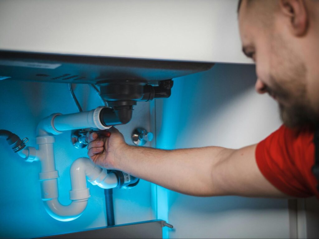 A plumber inspecting the pipes under a sink