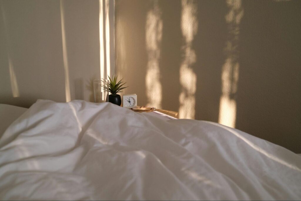 A bed covered in sheets with streaks of light on the wall behind it