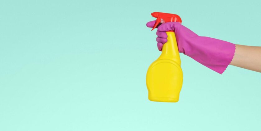 A hand with a rubber glove holding a cleaning solution