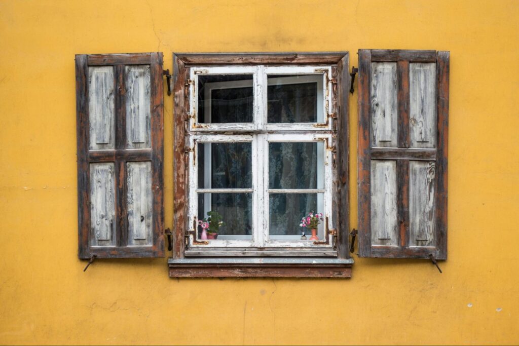 old window with shutters on a yellow wall