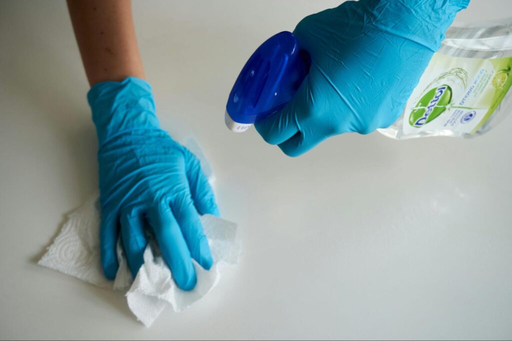 Person with blue gloves cleaning a white surface