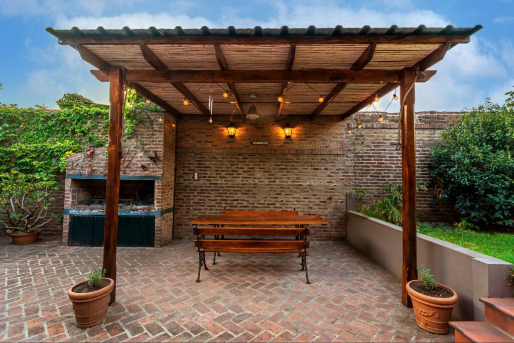 A pergola with a large dining table with a pizza oven on the side